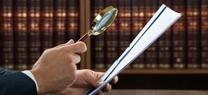 A white-collar worker using a magnifying glass to examine a document. Office supplies and equipment in the background. SEO: Businessperson using magnifier in office setting.