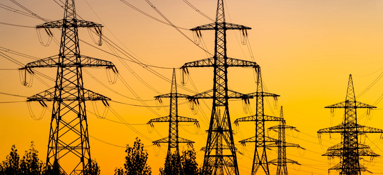 Linia elektroenergetyczna nadająca z wieżą przesyłową o zmierzchu, prezentująca pomarańczowe światło elektryczności w sieci elektroenergetycznej.