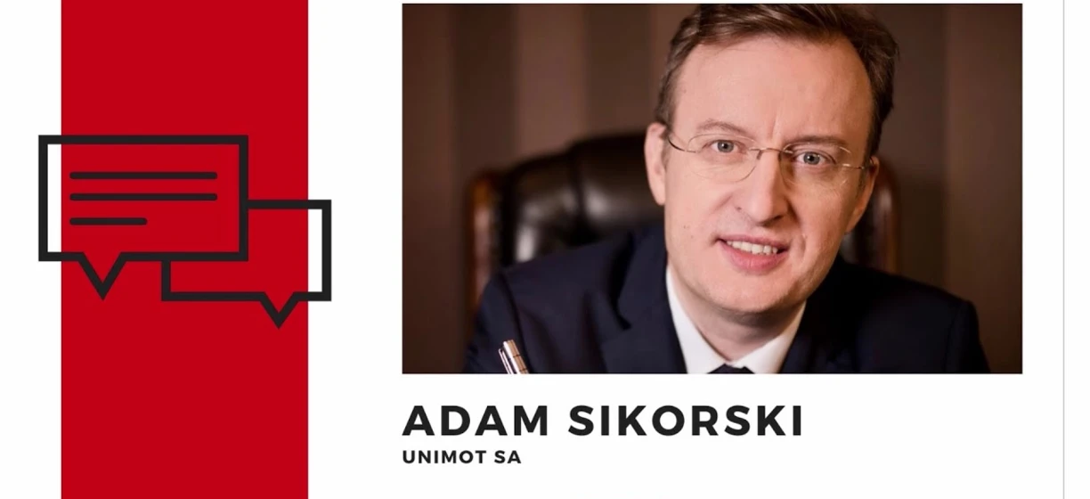 Profesjonalny mężczyzna w garniturze i okularach, zidentyfikowany jako Adam Sikorski z UNIMOT SA, w dyskusji biznesowej dla BIZNES ALERT.