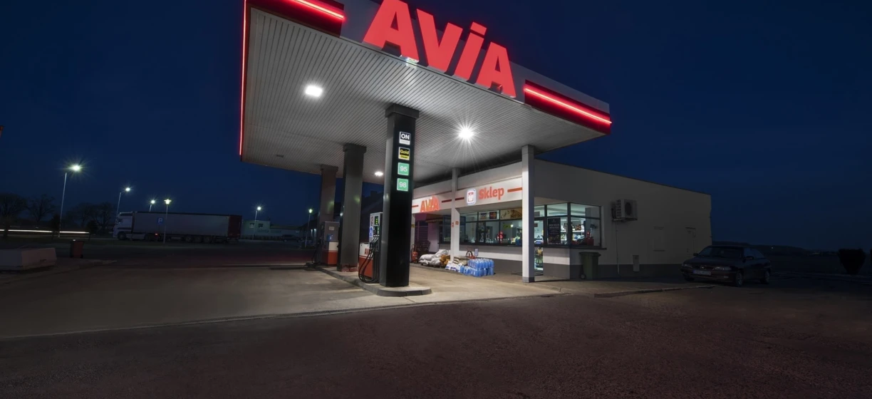 A fuel station sign in Polish displaying information about AVIA ON Gold 98 fuel. Includes a shop on site.