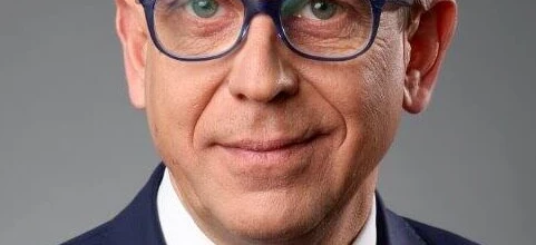 A person wearing glasses with chin resting on collar, cheek on hand, eyebrows slightly raised. Skin and forehead visible, emphasizing vision care.