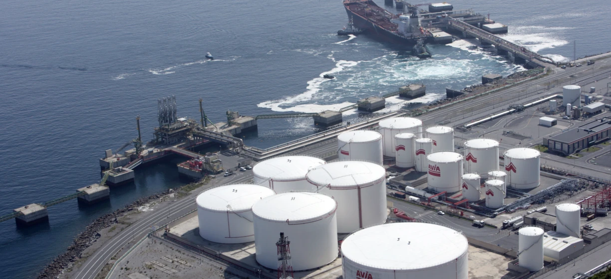 A bustling industrial scene with storage tanks, freight transport, and a power station by the port. AVIA and SD Eibar logos are prominently displayed.
