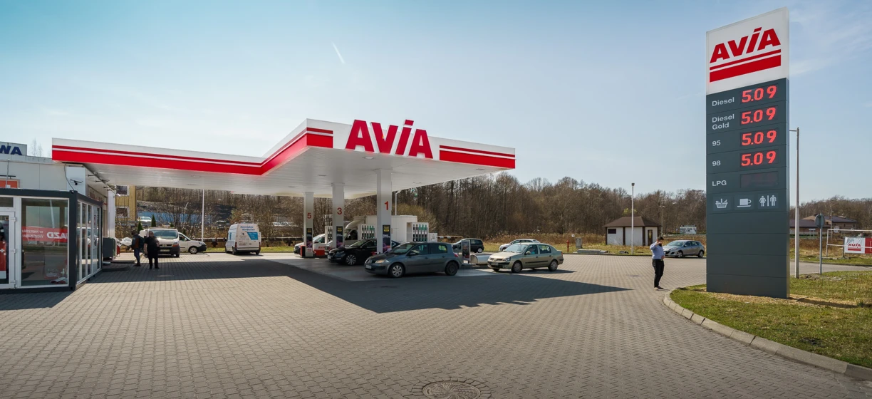 Image alt-text: A family car parked at a fueling station with a sport utility vehicle in the background. Fuel prices displayed for diesel, Gold 95, Gold 98, and LPG.