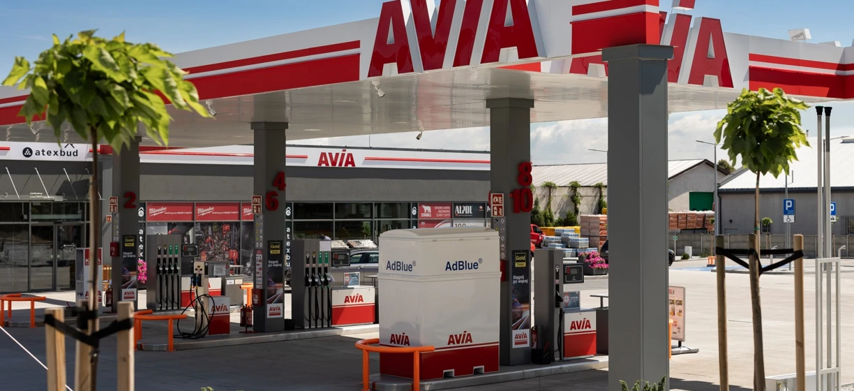 Gasoline truck at an AVIA filling station. Fuel dispenser and rear-view mirror visible on the hardtop SUV bumper. ATEXBUD and Mihranked logos prominent.