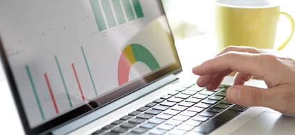 Tekst alternatywny: Osoba korzystająca z laptopa jako urządzenia wejściowego w ustawieniu biurowym. Na ekranie elektronicznego urządzenia wyświetla się ekran komputera z artykułami biurowymi w tle.