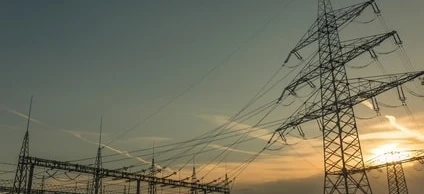 Overhead power line and transmission tower against a cloudy sky, symbolizing electricity and the public utility of the electrical network.