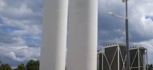 A composite material cylinder being inspected by an engineer in an industrial setting. Machinery and pipes in the background.