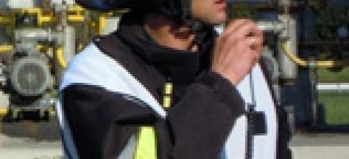 A blue-collar worker wearing personal protective equipment including a helmet and high-visibility clothing. The image shows an emergency service worker, possibly a firefighter, in their work uniform.