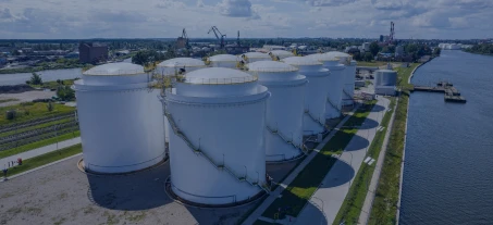 A tall storage tank silo reflecting in the water outside a factory in an industrial setting. Bright and clear day. Industry vibes.