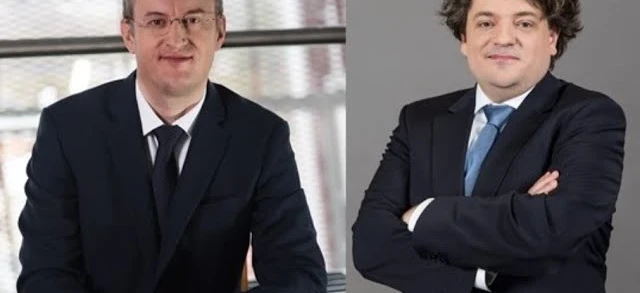 Mężczyzna w eleganckim garniturze i płaszczu pewnie stojący, z wydatnym kołnierzem otaczającym twarz i czoło. Klasyczny okrycie wierzchnie dla eleganckiego wyglądu.