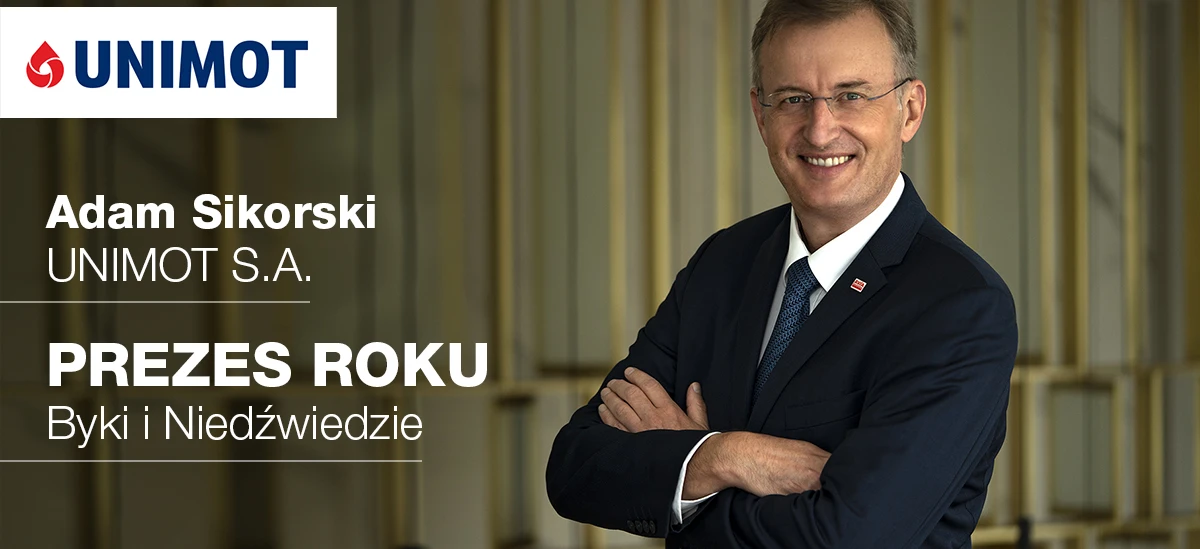 A formal wear-clad businessperson, wearing a blazer, dress shirt, and necktie, stands before a sign with Polish text honoring Adam Sikorski from UNIMOT S.A. as the CEO of the year. White-collar worker in professional attire.