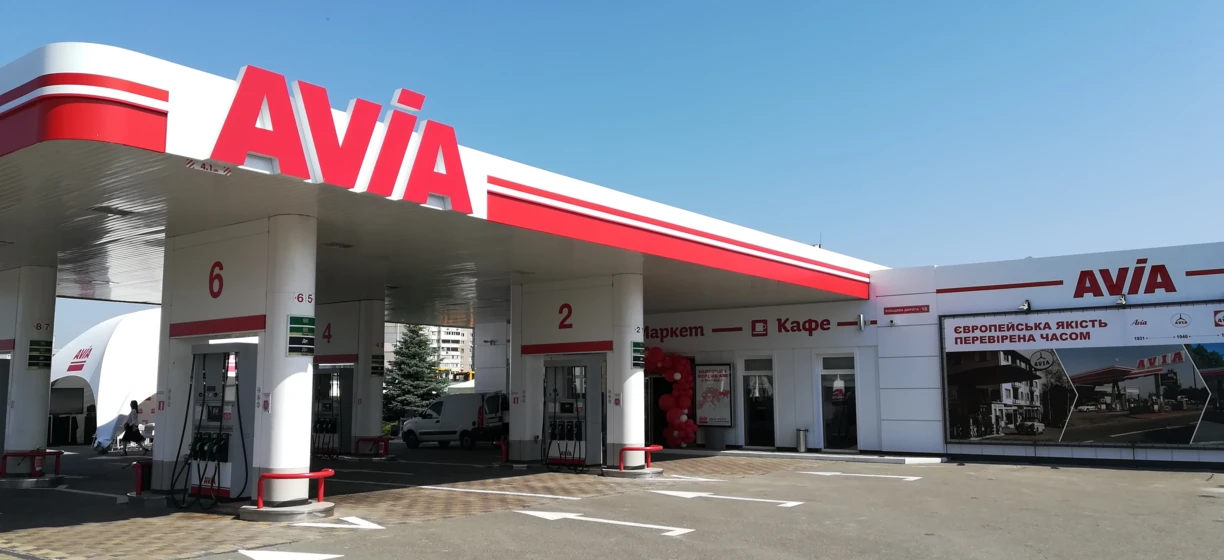 Alt-text: Automotive side-view mirror and bumper of a sport utility vehicle parked at a filling station. Image also shows rear-view mirror, hubcap, and car door with the AVIA brand logo.