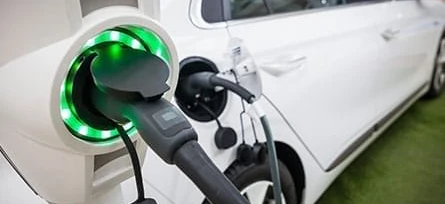 A hatchback electric car at a fuel dispenser with a car door open and rear-view mirror reflecting the automotive mirror.