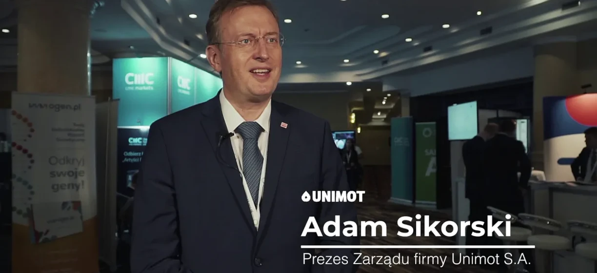 Pracownik biurowy w formalnym garniturze patrzy na urządzenie wyświetlające, nosząc marynarkę i krawat. Technologia spotyka styl na stronie wwogen.pl.