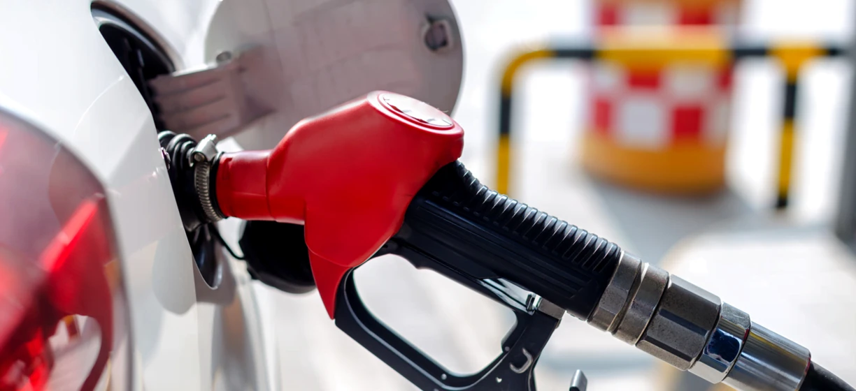A fuel dispenser at a filling station with a nozzle and hose, ready for gasoline or diesel fuel. An electric vehicle charging machine is also shown.
