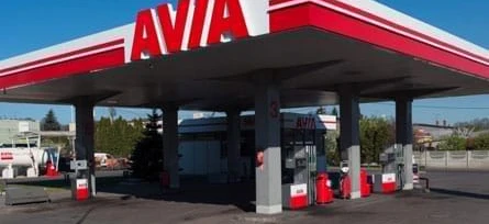 A car parked at a filling station with a shiny bumper and side-view mirror. Vehicle registration plate visible on the car door. AVIA logo on the hardtop.