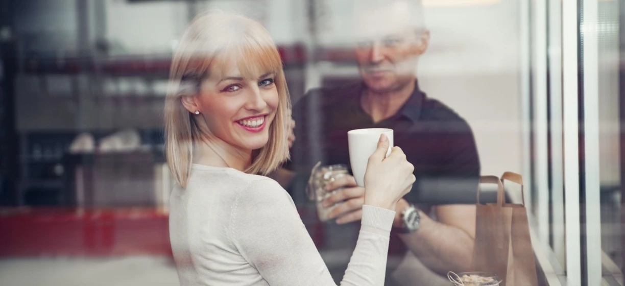 A woman with blond hair smiling while holding a coffee cup. Tableware and drinkware in focus, conveying happiness and enjoyment.