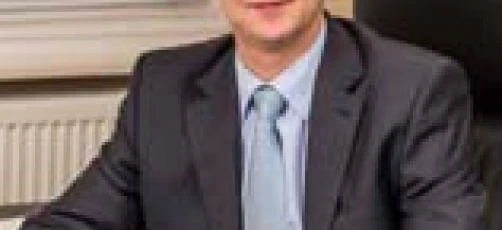 A businessperson in a formal suit and tie smiling with a professional facial expression. White-collar worker in a dress shirt and blazer.