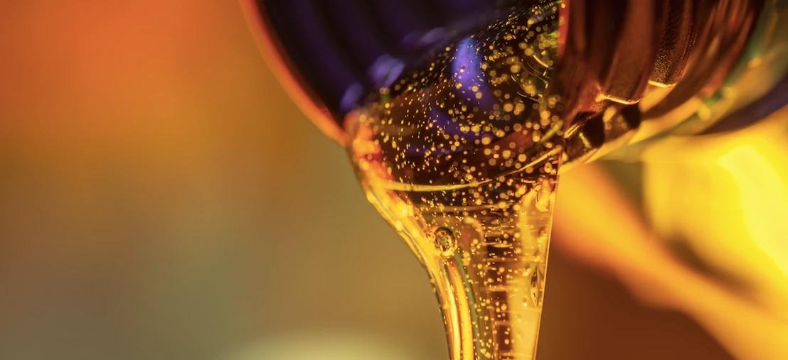 Close-up macro photography of flowing yellow and orange liquid resembling motor oil or cooking oil, with a focus on the texture and movement of the fluid.