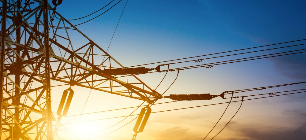 Linia przesyłowa oraz wieża przesyłowa z żółtymi i pomarańczowymi przewodami elektrycznymi, część publicznej sieci elektroenergetycznej.