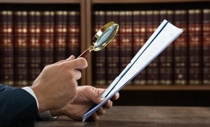 A white-collar worker using a magnifying glass to examine a document. Office supplies and equipment in the background. SEO: Businessperson using magnifier in office setting.