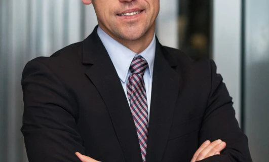 A man in formal wear smiles, wearing glasses with a collar and rolled-up sleeves. Vision care is important for a polished look.
