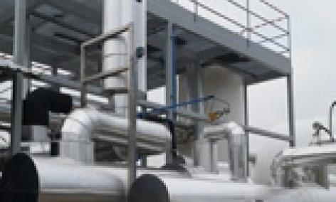 A close-up of a metal pipeline being manufactured by a machine in an industrial setting, made of composite materials. Iron and steel casing pipes are visible, showcasing the engineering processes involved.