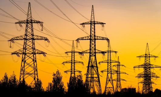 Linia elektroenergetyczna nadająca z wieżą przesyłową o zmierzchu, prezentująca pomarańczowe światło elektryczności w sieci elektroenergetycznej.