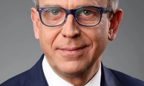 A person wearing glasses with chin resting on collar, cheek on hand, eyebrows slightly raised. Skin and forehead visible, emphasizing vision care.