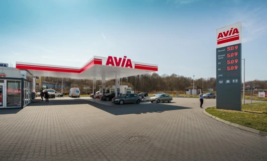 Image alt-text: A family car parked at a fueling station with a sport utility vehicle in the background. Fuel prices displayed for diesel, Gold 95, Gold 98, and LPG.