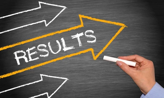 A desk cluttered with office supplies with a paper showing the word RESULTS, symbolizing productivity and success.