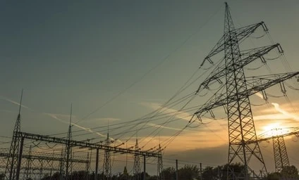 Overhead power line and transmission tower against a cloudy sky, symbolizing electricity and the public utility of the electrical network.