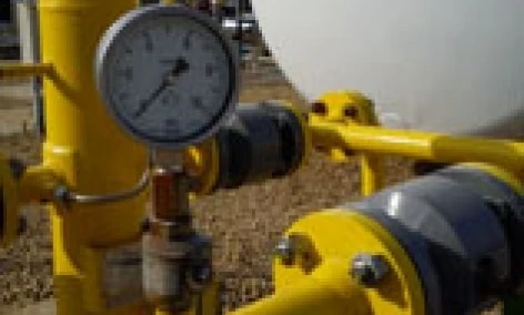 A industrial machine featuring a pipe, cylinder, and storage tank with plumbing valves and fittings made of steel. Measurements being taken on the equipment.