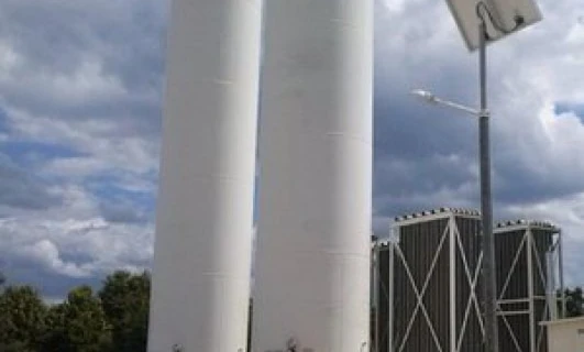 A composite material cylinder being inspected by an engineer in an industrial setting. Machinery and pipes in the background.