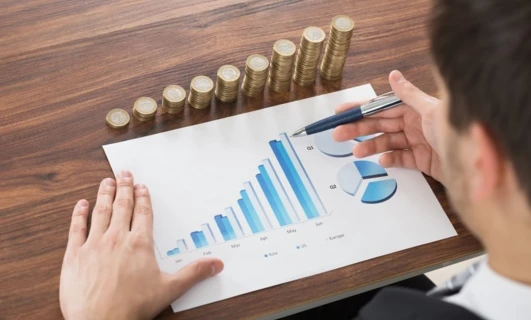 A businessperson's finger pointing at a diagram on a whiteboard in an office setting. Management gesture with thumb, office supplies and writing implement visible. Business planning for Jun, Feb, Ma, Apr, May, Q1 in Asia, US, Europe.