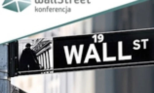 An aluminium street name sign on a wall, reading "WALL ST" and "Wall Street" in Polish language. The sign indicates the location of a conference at number 19 on Wall Street.