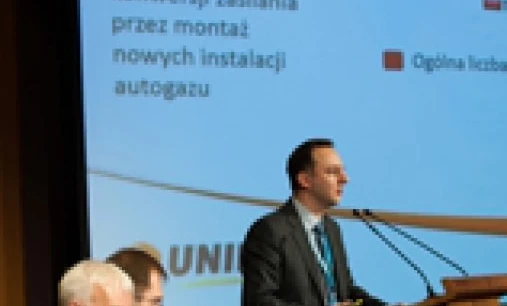 A spokesperson in a formal suit and coat is giving a speech at an event using audio equipment and a microphone. Text on the image mentions the total number of LPG conversions in 2012.
"Spokesperson in formal wear at an event discussing LPG conversions in 2012. Audio equipment and microphone visible."