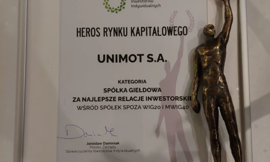 Nagroda dla Najlepszych Relacji Inwestorskich wśród firm spoza WIG20 i MWIG40. Przyznana UNIMOT S.A. przez Stowarzyszenie Inwestorów Indywidualnych. Jarosław Dominiak, Prezes Stowarzyszenia, przyjmuje trofeum na podium z mosiężną banderą.
