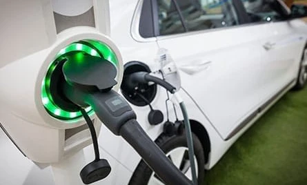 A hatchback electric car at a fuel dispenser with a car door open and rear-view mirror reflecting the automotive mirror.