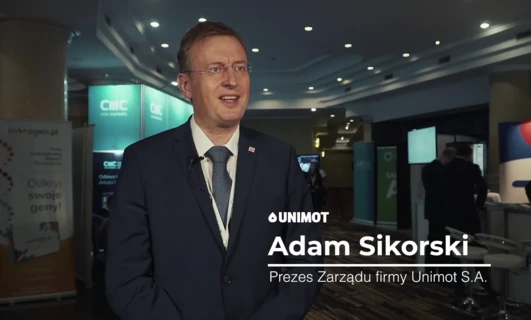 Pracownik biurowy w formalnym garniturze patrzy na urządzenie wyświetlające, nosząc marynarkę i krawat. Technologia spotyka styl na stronie wwogen.pl.