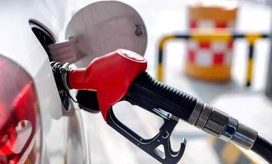 A fuel dispenser at a filling station with a nozzle and hose, ready for gasoline or diesel fuel. An electric vehicle charging machine is also shown.