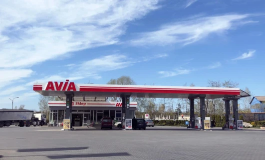 Samochód rodzinny zaparkowany na stacji paliw z widokiem na lustro boczne i zderzak samochodowy. Słowa kluczowe: AVIA, Sklep, MEGA, paliwo, parking samochodowy.