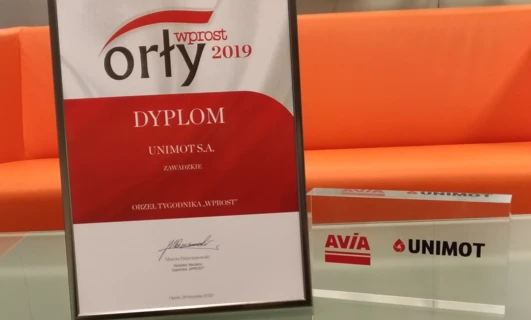 Zdjęcie przedstawiające pomarańczową etykietę z tekstem w różnych czcionkach, w tym logo czasopisma wprost. Przyznane Marcinowi Dzierzanowskiemu z UNIMOT S.A. za rok 2019.