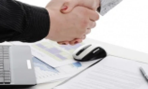 Two white-collar workers are shaking hands in an office setting, symbolizing a greeting or agreement between colleagues. The gesture signifies professionalism and collaboration in a meeting or discussion about management and job-related topics.