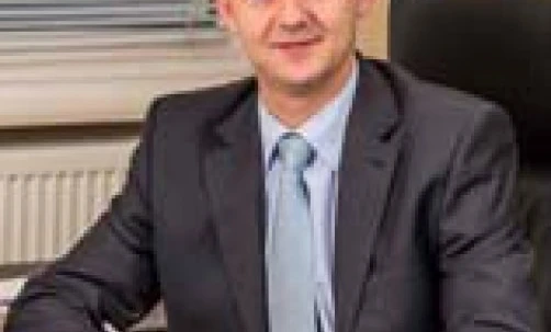 A businessperson in a formal suit and tie smiling with a professional facial expression. White-collar worker in a dress shirt and blazer.