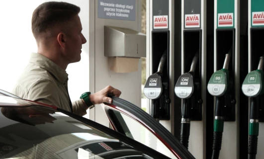 Dystrybutor paliwa na stacji benzynowej z luksusowym samochodem zaparkowanym przy dystrybutorze. Słowa kluczowe: Paliwo, Benzyna, Pojazd elektryczny, Maszyna.