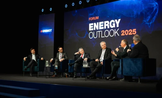 A white-collar worker in a suit stands on stage at an event, with the UNIMOT logo in the background. Technology and advertising play a key role in this convention showcasing the energy outlook for 2025.