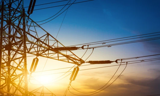 Linia przesyłowa oraz wieża przesyłowa z żółtymi i pomarańczowymi przewodami elektrycznymi, część publicznej sieci elektroenergetycznej.
