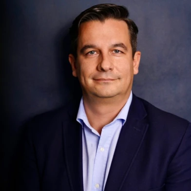 Зблизька фотографія особи, яка показує своє посміхаюче обличчя з каштановим волоссям і рукавом, що торкається кадру.