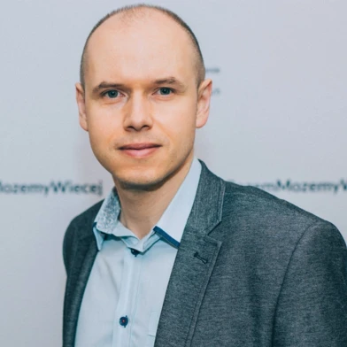 Чоловік у формальному піджаку та сорочці з серйозним виразом обличчя, рука на комірі і лобом, опираючись на рукав, символізуючи визначеність і увагу. Польський текст: "Możemy więcej" перекладається як "Ми можемо більше".